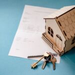 Modellhaus steht auf einer Rechnung. Im Vordergrund liegen Wohnungsschlüssel.
